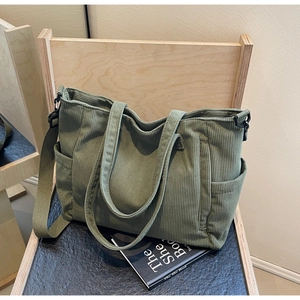 Detail of green corduroy tote bag showing side pocket and detachable strap on a wooden chair