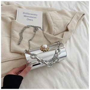 Detail of silver cylindrical clutch with pearl clasp and dual chain straps on blazer