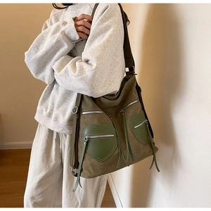 Close-up of olive green corduroy hobo bag featuring heart-shaped zipper pockets and tassels