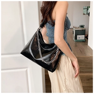 Detail of glossy black leather tote bag with thick silver chain on a model shoulder