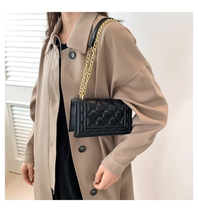 Close-up of heart-shaped quilted stitching and gold chain strap on black shoulder bag