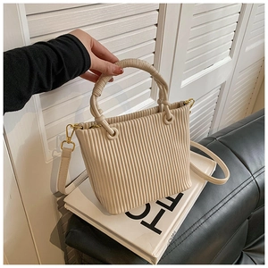 Detail of beige pleated bucket bag featuring vertical ridges and gold metal hardware