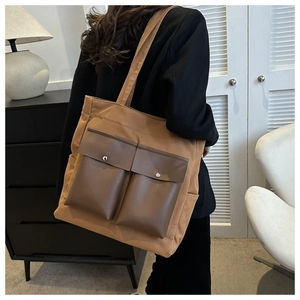 Brown canvas tote bag with front leather pockets and silver buttons on model side view