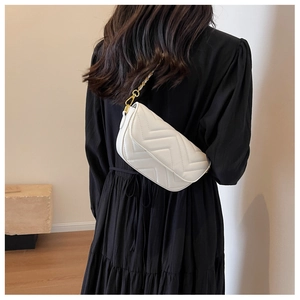 Detailed shot of white quilted shoulder bag with V-shaped stitching and gold chain strap
