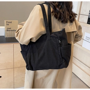 Side view of a black corduroy tote bag worn over the shoulder with a khaki trench coat