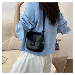 Detail of a black crossbody bag with vertical pleated texture and oval decorative buckle