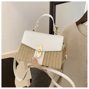 Nahaufnahme einer Strohtasche mit weißem Lederbesatz und goldenem rechteckigem Schloss