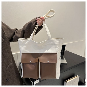 Detail of canvas tote bag showing two brown leather flap pockets with metal snap buttons