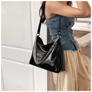 Detail of a black leather tote bag with thick silver chain on a model in a minimal setting