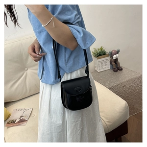 Fashionable black matte leather saddle bag shown on model in a stylish home setting