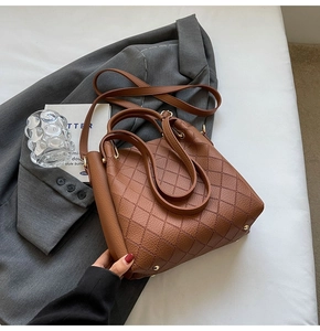 Detailed view of caramel brown quilted leather bucket bag with top handle and metal base feet