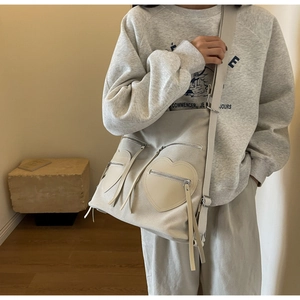 Detail of beige canvas crossbody bag featuring two heart-shaped leather zipper pockets