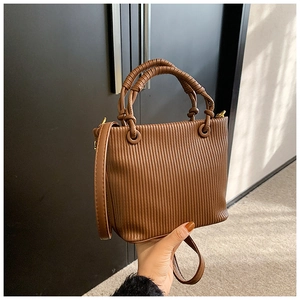 Detail of brown pleated bucket bag with vertical texture and golden hardware accents