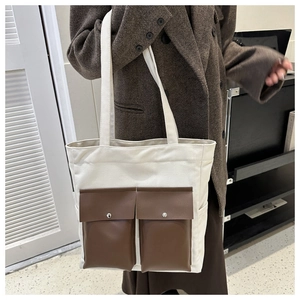 Detail of a large canvas tote bag with brown leather front pockets on an autumn coat