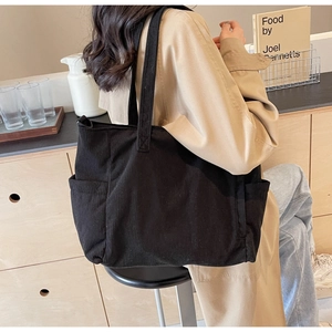 Detail of a black corduroy tote bag showing large capacity and textured fabric on shoulder