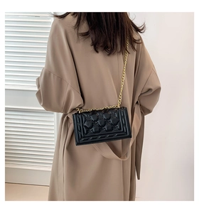 Detail of black quilted leather shoulder bag with gold chain strap worn by a model