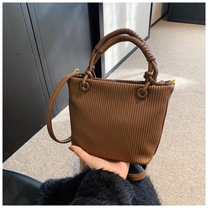 Detail of dark brown pleated bucket bag with a woven handle and textured vertical stripes