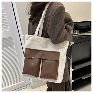 Detail view of large white canvas tote bag with brown leather front snap pockets