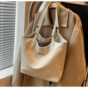 Detail of minimalist cream tote bag in lychee pattern leather hanging on a trench coat