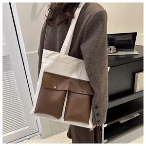 Detail of the large canvas tote bag featuring two brown leather front pockets with metal snaps