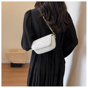 Detail of white quilted crossbody bag with gold chain strap shown on a model