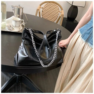 Detail view of large black leather tote bag with silver chunky chain strap on a table