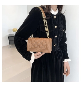 Detail of a brown quilted handbag with heart pattern stitching and gold chain strap