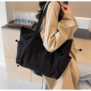 Close-up of black corduroy tote bag showing large side pocket and ribbed fabric texture
