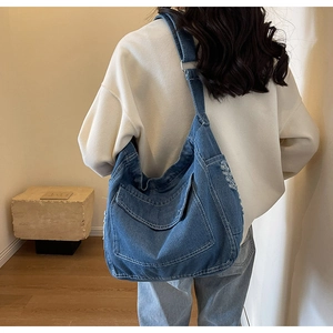 Dettaglio di una grande borsa a tracolla in denim con cuciture bianche e ampie tasche