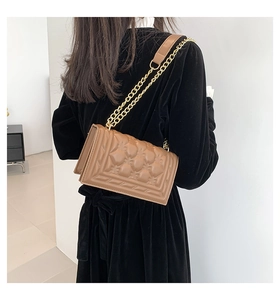 Detail of a brown quilted leather crossbody bag with a chunky gold chain strap on a model