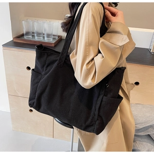Detail of black corduroy tote bag showing side pocket and soft vertical ribbed texture