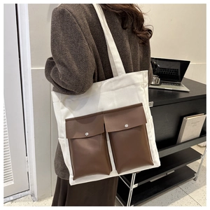 Detail of off-white canvas tote bag featuring dual brown faux leather front pockets with snaps