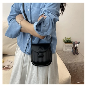 Detail of black pleated saddle bag with crossbody strap shown in a lifestyle setting
