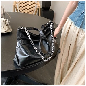 Detailed view of black glossy tote bag with silver chain strap on a cafe table
