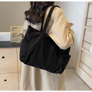 Detail view of large black corduroy tote bag showing vertical texture and side pocket