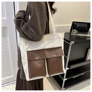Detail view of canvas tote bag with brown front pockets and snap metal button closure