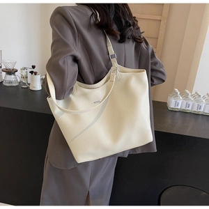 Detailed view of beige lychee leather tote bag with adjustable strap and metal logo