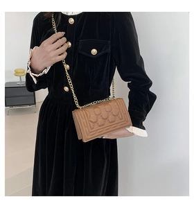 Brown quilted leather shoulder bag with gold chain strap worn by a woman in a black dress