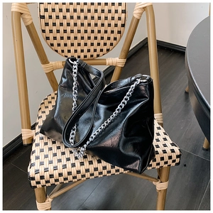Close-up of black glossy leather tote bag with silver chain detail on a woven chair