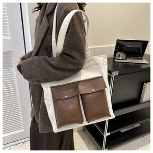 Detail view of canvas tote bag with brown leather front pockets and metal snaps
