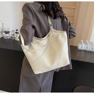 Detail view of cream leather tote bag featuring rich lychee texture and dual strap design