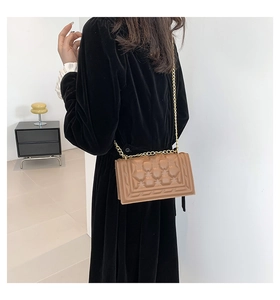 Detail of a brown leather crossbody bag with geometric texture and gold chain strap