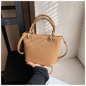 Detail of light brown pleated bucket bag with a woven knot handle and metal strap hooks