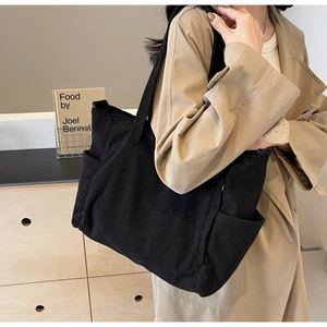 Detail of black corduroy tote bag showing side pocket and spacious texture on model