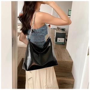 Detailed view of black patent leather hobo bag with silver chain strap worn on shoulder