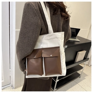 Detail of white canvas tote bag featuring brown faux leather front pockets with metal snaps