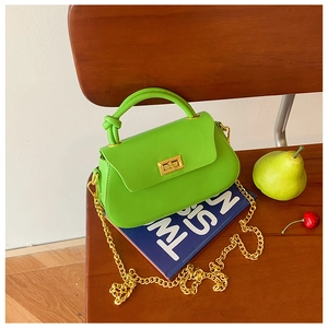 Detail of neon green leather handbag with gold chain strap on a wooden chair and book
