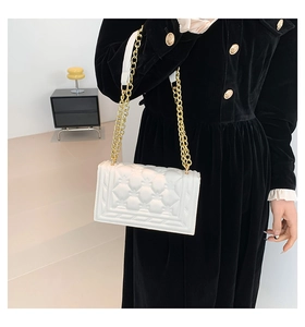 Close-up of white quilted PU leather handbag with elegant golden metal chain straps