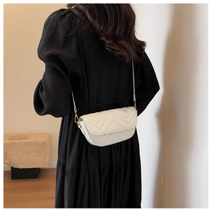Close-up of white V-quilted leather saddle bag with gold metal hardware on model