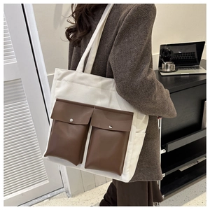 Detail of canvas tote bag with brown leather pockets and metal snaps on model